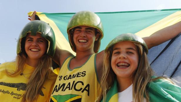 Drei Jugendliche mit Wassermelonenhelmen und Jamaika-Flagge lächeln in die Kamera.