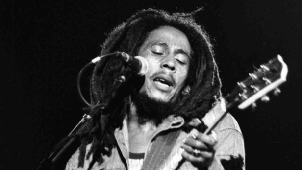 Bob Marley singt mit Dreadlocks in ein Mikrofon und spielt Gitarre.
