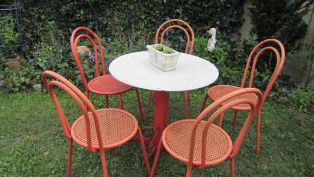 Ein roter Gartentisch mit Stühlen steht im Grünen.