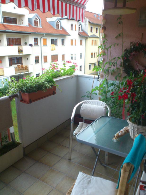 Ein mit Blumen und Pflanzen dekorierter Balkon mit Tisch und Stühlen.