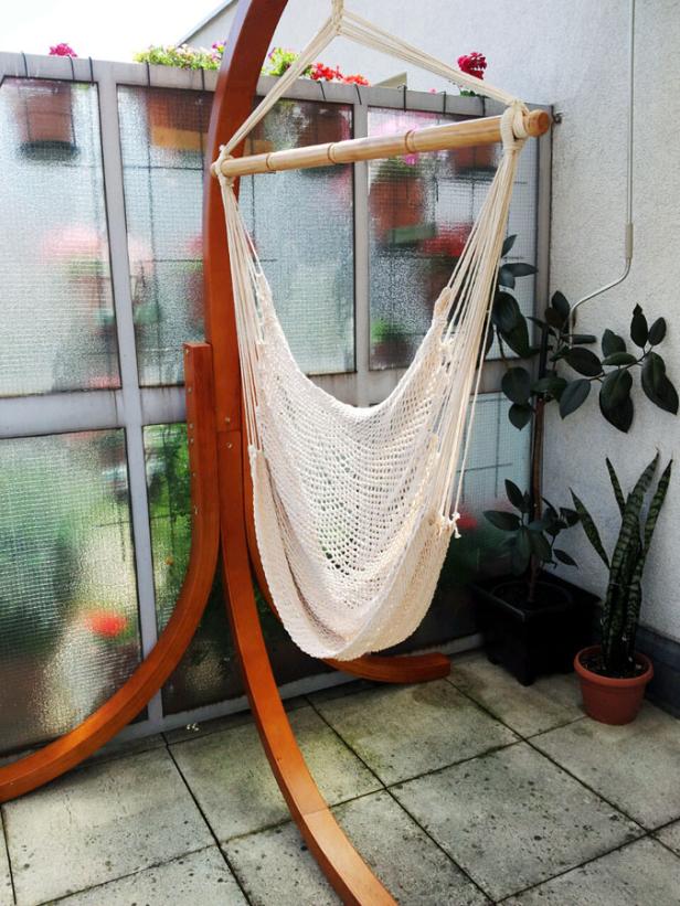 Eine hängende Makramee-Hängematte steht auf einer Terrasse.