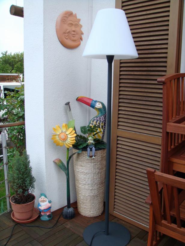 Eine Stehlampe und Gartendekorationen stehen auf einer Terrasse.