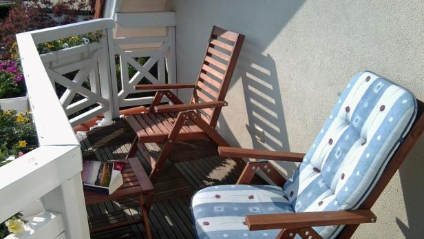 Zwei Holzstühle und ein Beistelltisch mit einem Buch auf einem sonnigen Balkon.