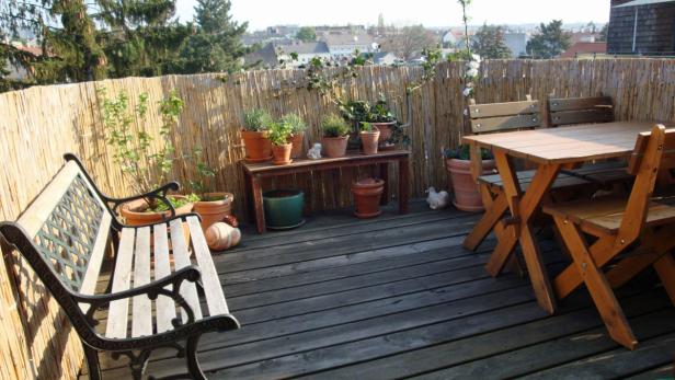 Eine Terrasse mit Holzboden, einer Bank, einem Tisch und vielen Blumentöpfen.