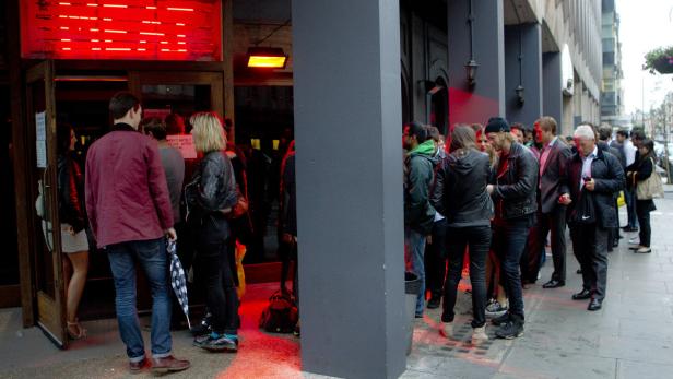 Menschen stehen vor einem Gebäude mit roter Beleuchtung Schlange.