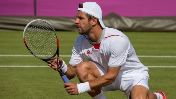 Ein Tennisspieler mit weißer Kappe kniet auf dem Rasen und hält einen Tennisschläger.