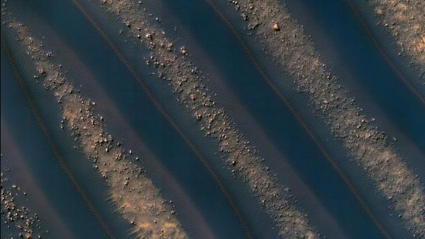 Luftaufnahme von dunklen Sanddünen mit helleren Ablagerungen.