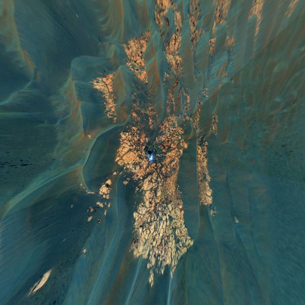 Blick von oben auf eine felsige Landschaft mit einem kleinen Gebäude mit blauer Beleuchtung.