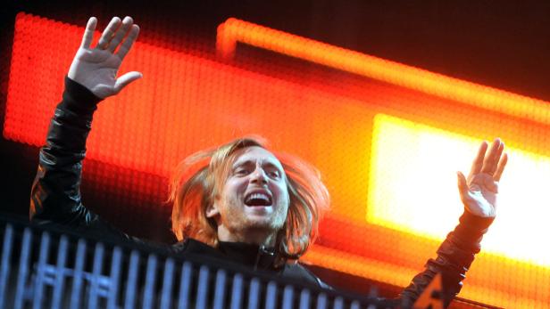 David Guetta legt bei einem Konzert auf und reißt die Arme hoch.