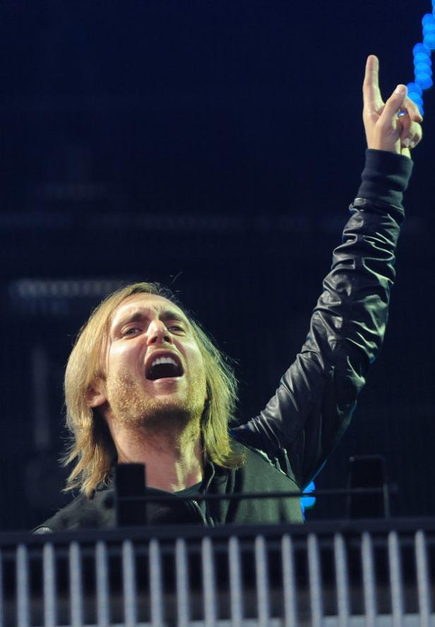 David Guetta legt bei einem Konzert auf und reckt einen Arm in die Höhe.
