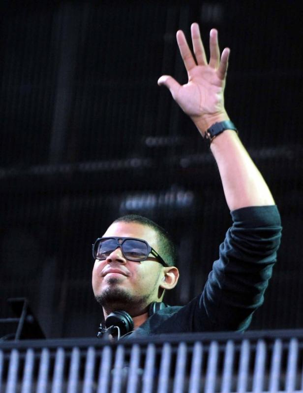 Ein DJ mit Sonnenbrille und Kopfhörern hebt die Hand.