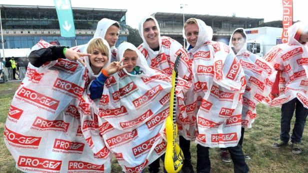 Eine Gruppe junger Leute in Regenponchos mit der Aufschrift „PRO-GE“ posiert für ein Foto.