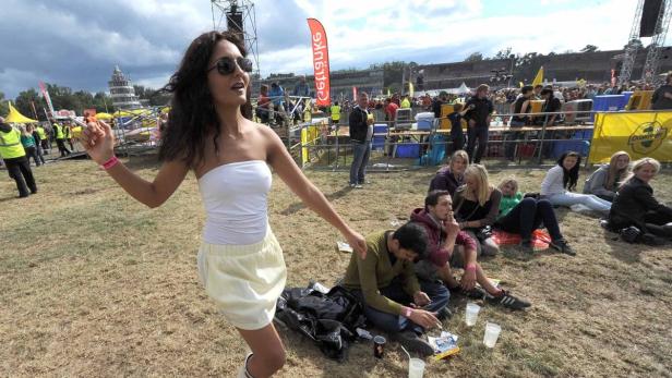 Eine junge Frau tanzt auf einem Festivalgelände vor einer Menschenmenge.