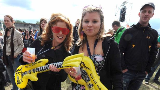Zwei Frauen halten aufblasbare Gitarren und Getränke auf einem Musikfestival.