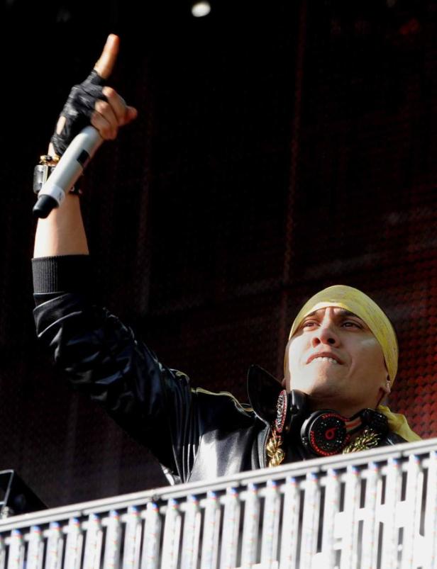 Ein Mann mit gelbem Stirnband und Kopfhörern hält ein Mikrofon in die Höhe.