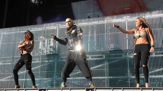 Ein Mann in Sportkleidung steht mit zwei Tänzerinnen auf einer Bühne.