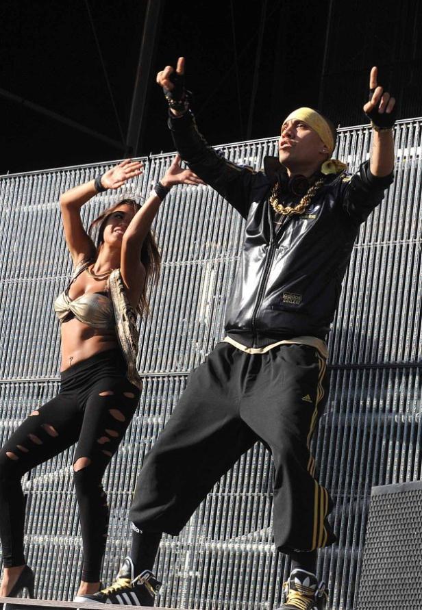 Ein Mann mit Goldkette und eine Frau tanzen vor einem Gitter.