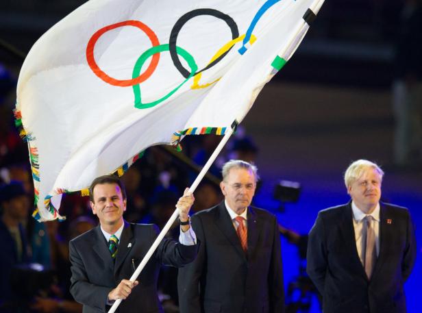 Drei Männer tragen die olympische Flagge.