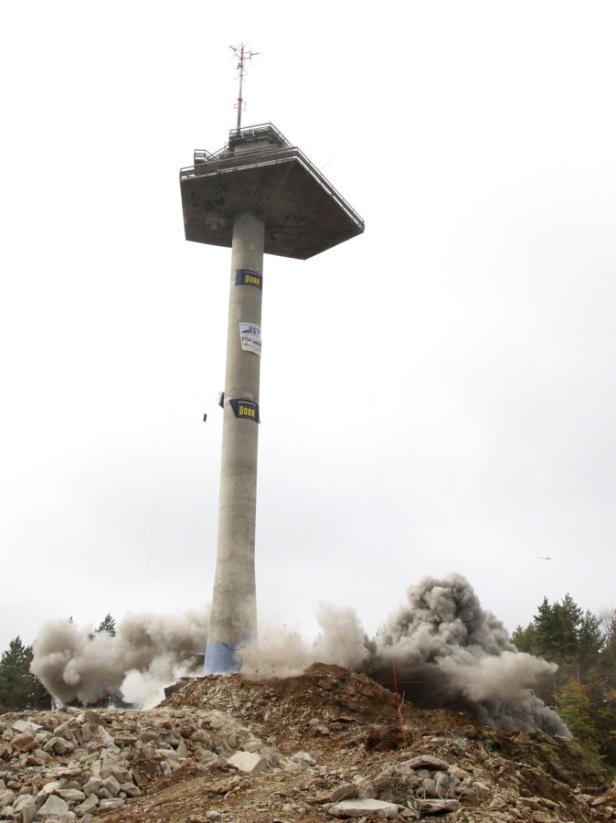 Ein hoher Turm wird gesprengt, Staub und Trümmer fliegen durch die Luft.