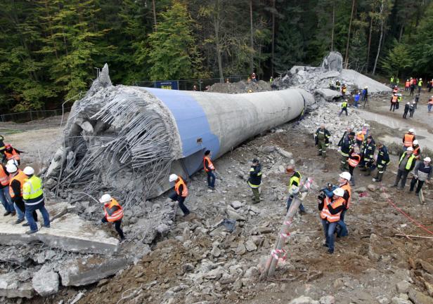 Ein eingestürztes Windrad liegt auf einem Trümmerfeld, umgeben von Rettungskräften.