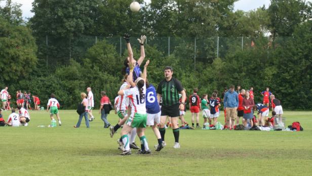 Eine Gruppe von Frauen spielt Gaelic Football auf einem grünen Feld.