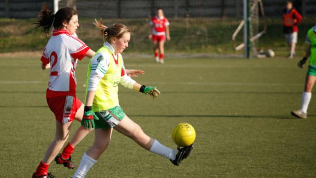Eine junge Frau spielt Gaelic Football auf einem grünen Feld.