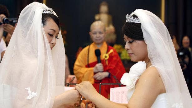 Zwei Frauen in Brautkleidern tauschen Ringe während einer buddhistischen Zeremonie.