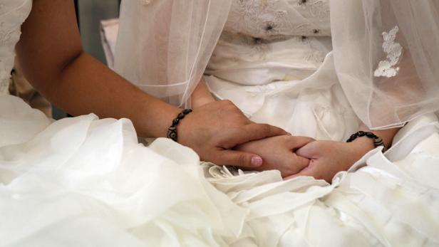 Eine Braut im weißen Kleid hält ihre Hände mit Armbändern.