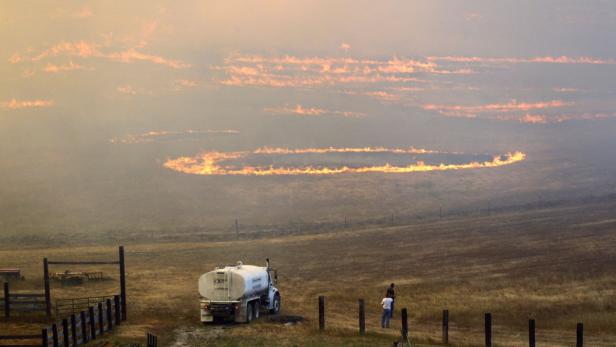 Ein Feldbrand erzeugt eine Rauchwolke am Himmel, während ein Tankwagen bereitsteht.