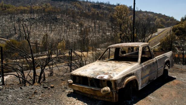 Ein ausgebrannter Pickup-Truck steht vor einer durch ein Feuer verwüsteten Landschaft.