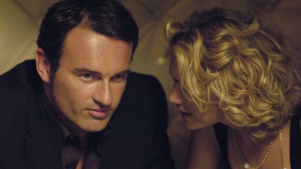 Ein Mann im Anzug und eine Frau mit blonden Locken unterhalten sich.