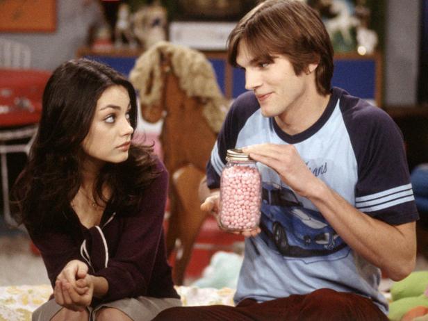Ashton Kutcher hält ein Glas mit rosa Süßigkeiten, während Mila Kunis ihn ansieht.