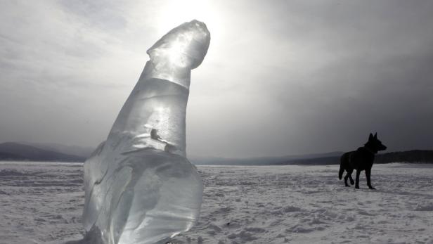 Eine Eisskulptur steht auf einer verschneiten Fläche, im Hintergrund ein dunkler Hund.