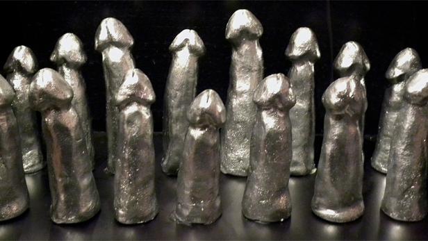 Eine Ansammlung silberner Penis-Statuetten steht auf einer schwarzen Oberfläche.
