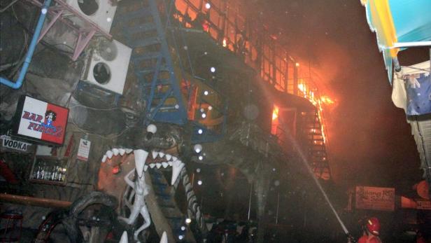 Ein Gebäude steht in Flammen, während ein Feuerwehrmann es mit einem Schlauch zu löschen versucht.