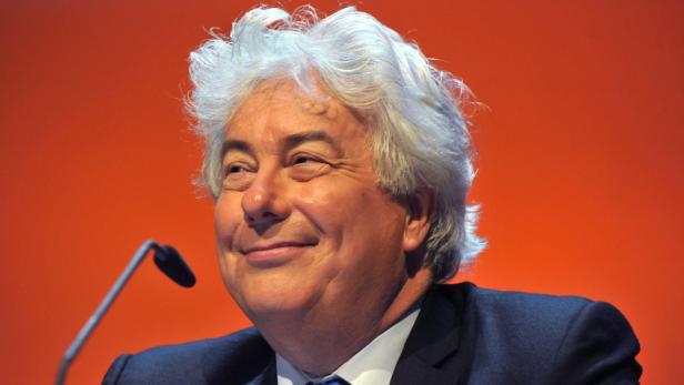 Ein Mann mit weißem Haar lächelt vor einem orangefarbenen Hintergrund.