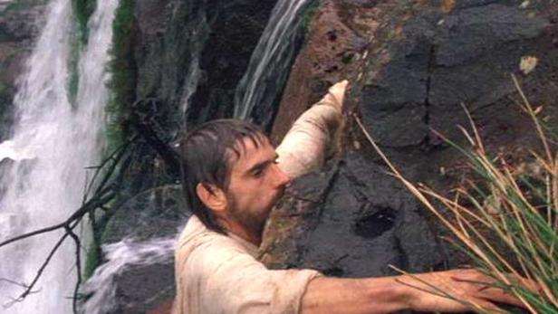 Ein Mann klettert an einem Felsen neben einem Wasserfall.