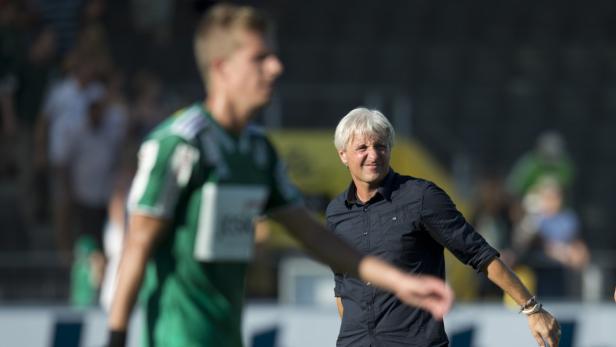 Ein Fußballtrainer mit grauem Haar steht am Spielfeldrand.