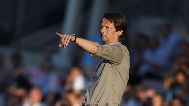 Ein Mann in einem grauen Hemd zeigt mit dem Finger nach links.