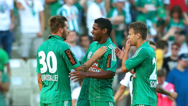 Drei Fußballspieler in grünen Trikots feiern gemeinsam auf dem Spielfeld.