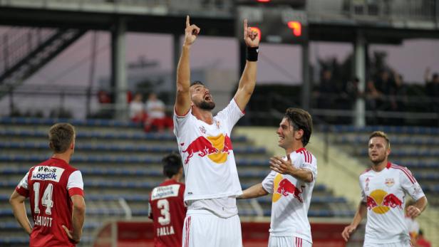 Ein Fußballspieler jubelt mit erhobenen Armen, während seine Teamkollegen ihn anfeuern.