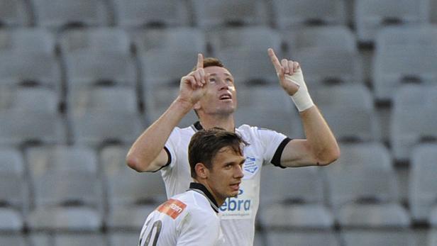 Ein Fußballspieler jubelt mit erhobenen Zeigefingern, ein anderer steht im Vordergrund.