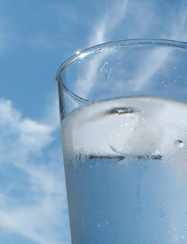 Ein Glas kaltes Wasser mit Eiswürfeln vor blauem Himmel.