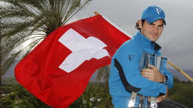 Roger Federer hält eine Trophäe vor einer Schweizer Flagge.