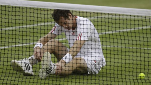 Ein Tennisspieler sitzt erschöpft auf dem Platz hinter dem Netz.