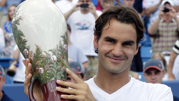 Roger Federer hält eine große Trophäe mit Tennisballdekor in den Händen.