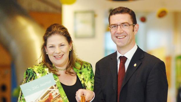Eine Frau mit einem „ZAG Journal“ und ein Mann im Anzug lächeln in die Kamera.