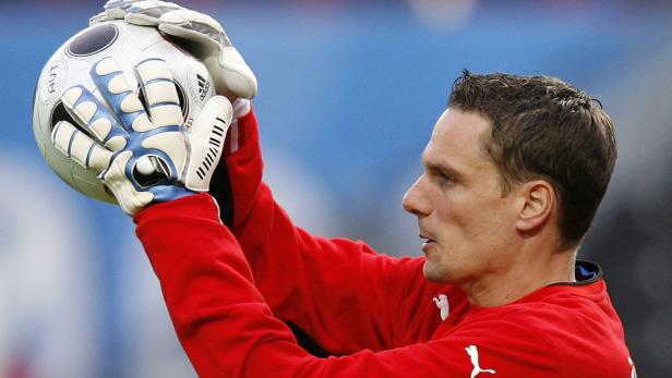 Ein Torwart hält einen Fußball mit seinen Handschuhen hoch.