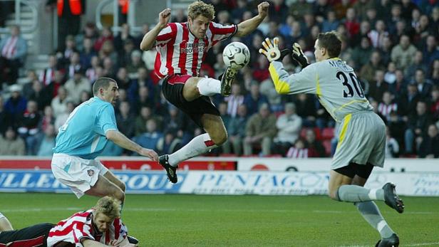 Ein Fußballspieler springt, um den Ball vor dem Torwart zu spielen.