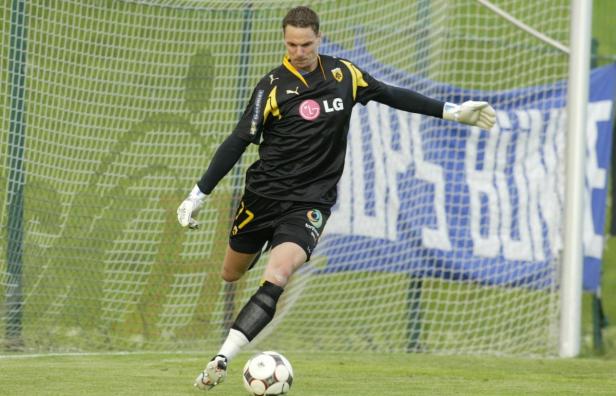 Ein Fußballtorwart in schwarzer und gelber Sportkleidung schießt einen Fußball.